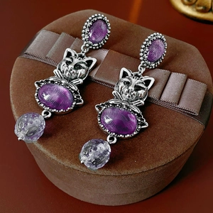Macro detail of vintage cat earrings in antique silver with purple gems on velvet box