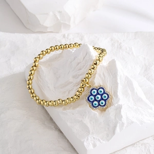 18K gold-plated beaded bracelet with blue evil eye zircon pendant on stone background