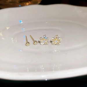 Close-up of golden flower stud earrings with sparkling cubic zirconia on a white plate