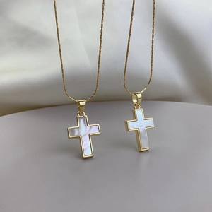 Close-up of gold cross pendant with white mother of pearl inlay on silk background