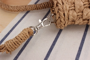 Detail of silver metal spring clasp connecting the woven straw strap and handbag body