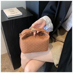 Detail view of a brown woven texture handbag featuring a gold metal lock and structured design