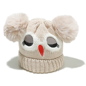 Close-up of beige knitted baby hat featuring embroidered owl face and twin fluffy pom-poms