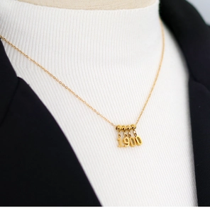 Close-up of golden number 1900 pendant on a minimalist chain worn on a black blazer