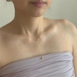 Detail showing a gold Y-shaped necklace with a zircon accent and round bead pendant