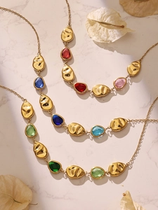 Detail of gold necklaces featuring colorful teardrop crystals on marble background