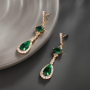 Macro detail of long emerald green teardrop earrings with gold setting and white zircons