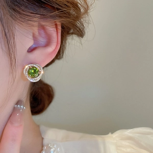 Close-up of golden spiral earrings with a green gemstone and micro-pave crystals on a model