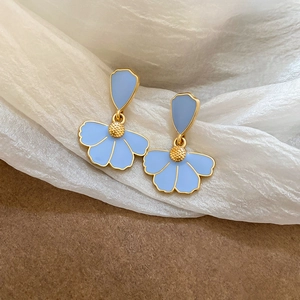 Detail of blue petal earrings with gold edges on white silk and brown background