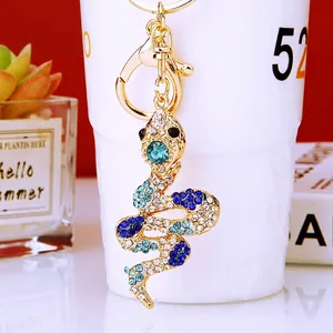 Golden snake keychain with blue rhinestones and crystals hanging on a ceramic cup