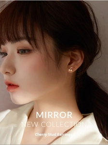Close-up of a small gold cherry earring on a model's ear with delicate details