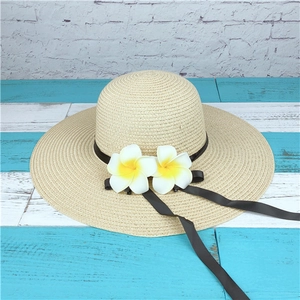 Detail of beige woven straw sun hat with realistic frangipani flowers and black ribbon