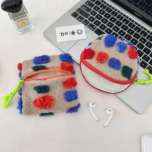 Close-up of plush pouch with colorful dots, orange zipper and green strap on a desk