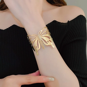 Close-up of a wide gold butterfly cutout open bangle worn on a woman's wrist