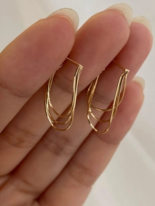 Close-up of golden multi-layer snake chain tassel earrings held by hand for detail