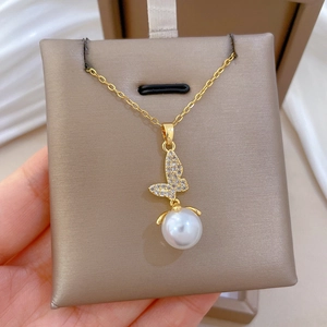 Detailed view of a gold butterfly pearl pendant necklace held over a beige jewelry box