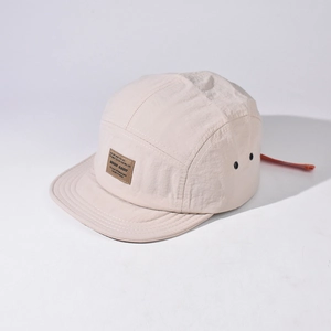 Detailed macro view of beige nylon 5-panel hat with leather logo patch and metal eyelets