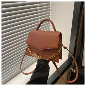 Detailed view of brown crossbody bag with gold chain decoration and crocodile texture