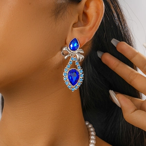 Close-up of bow earrings with teardrop blue stones on model, vintage court style design