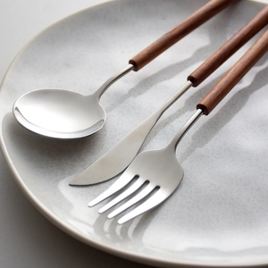 3-piece 304 stainless steel cutlery set with pear wood handles on a ceramic plate