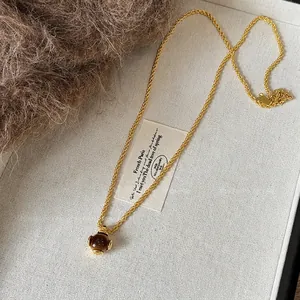 Macro shot of tiger eye teardrop pendant with gold chain on minimalist fabric tray