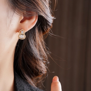 Detailed close-up of a model wearing a gold gourd-shaped earring with sparkling zircons