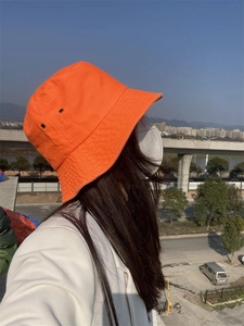 Orange cotton bucket hat with metal eyelets detail worn in a bright city setting