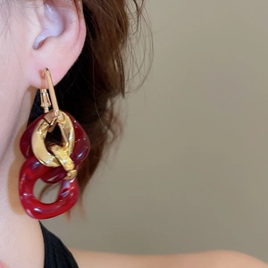 Detail of burgundy resin and polished gold metal chain earrings worn on ear