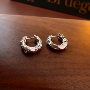Detail showing silver hoop earrings with irregular hammered texture on dark wood background