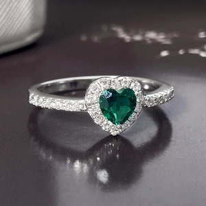 Elegant heart-shaped green gemstone ring with a halo of sparkling stones on a gray background