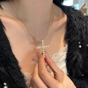 Close-up of a gold cross pendant necklace featuring shimmering white round-cut crystals