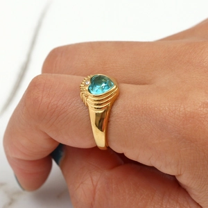 Detail of a gold plated heart ring with a blue gemstone on a marble background