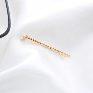 Close-up of golden moon-shaped hair clip with three inlaid rhinestones on white fabric