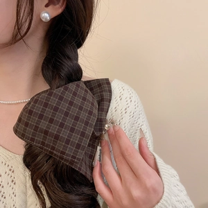 Detail of a brown plaid fabric bow scrunchie with a handmade tag on a braided hairstyle