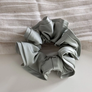 Macro detail of glossy sage green satin scrunchie with elegant ruffled texture