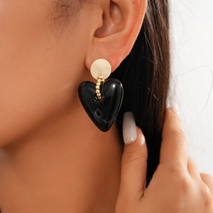 Macro detail of acrylic black heart pendant earring with gold stud on model