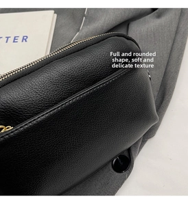 Close-up of black lychee grain leather crossbody bag with golden dual metal zippers