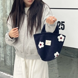 Detail of navy plush knit tote bag featuring 3D white flower appliques and brand label