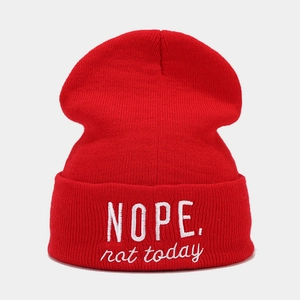 Close-up of red knit beanie featuring white embroidered NOPE text and ribbed texture