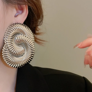 Detailed view of silver metallic spiral earring with textured circular pattern on model