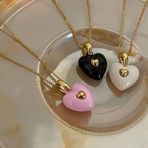 Macro shot of three vintage enamel heart necklaces in pink, black, and white on a glass tray