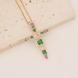 Gold-plated cross pendant necklace with colorful gemstones on a beige stone surface