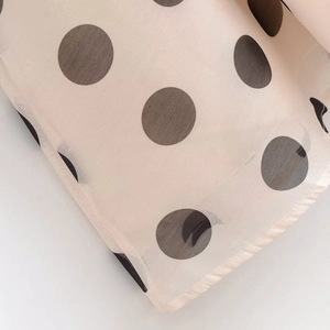 Gros plan sur le tissu mousseline beige à pois noirs montrant la texture fluide