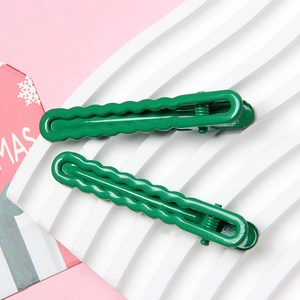 Macro shot of two green metal hair clips with wavy texture on a white tray