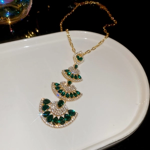Detail of gold fan pendant necklace with green teardrop stones and pavé set crystals