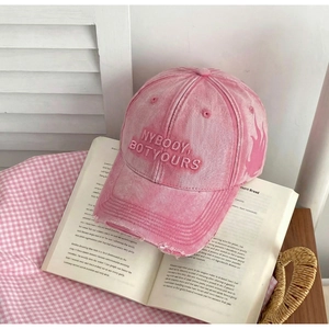 Close-up of pink washed cotton baseball cap with distressed brim and 3D letter embroidery