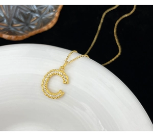 Macro shot of gold letter C pendant with textured surface and pavé white zircons