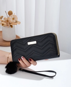 Close-up of black long wallet with V-shaped quilting, gold hardware, and pom-pom charm