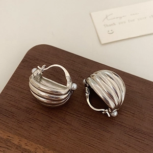 Detail of silver ribbed croissant earrings with pearl accents on dark wood background