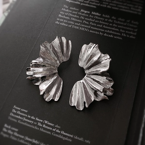 Détail macro de boucles d'oreilles argentées à plis métalliques et texture brossée